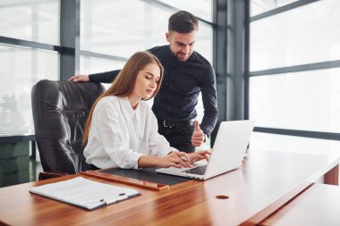 Resmi giyinmiş bir kadın ve bir adam ofis içinde masa başında birlikte çalışıyorlar..