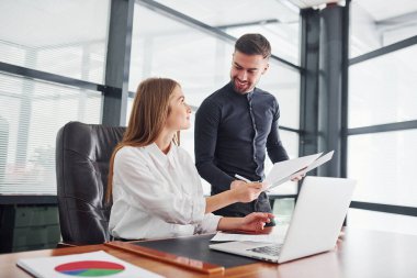 Resmi giyinmiş bir kadın ve bir adam ofis içinde masa başında birlikte çalışıyorlar..
