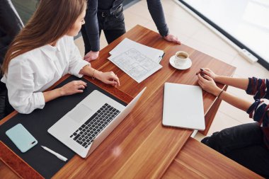 Ofiste laptopla ve belgelerle çalışan üç kişinin üst görüntüsü.