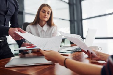 Resmi giyinmiş bir kadın ve bir adam ofis içinde masa masa dokümanlarla birlikte çalışıyorlar..