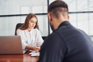Belgelerle oturan adam. Resmi giyinmiş bir kadın ve bir adam ofis içinde masa başında birlikte çalışıyorlar..