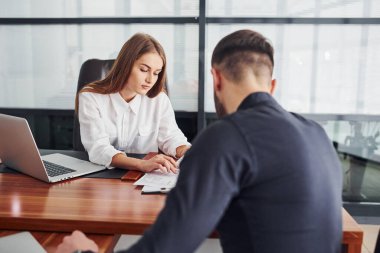 Belgelerle oturan adam. Resmi giyinmiş bir kadın ve bir adam ofis içinde masa başında birlikte çalışıyorlar..