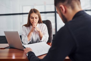 Belgelerle oturan adam. Resmi giyinmiş bir kadın ve bir adam ofis içinde masa başında birlikte çalışıyorlar..