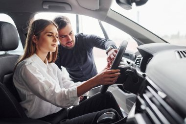 Kadın, salonda erkek asistanın yardımıyla arabayı test ediyor..