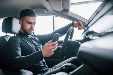 Zarif elbiseli bir adam yepyeni pahalı bir arabada oturuyor..