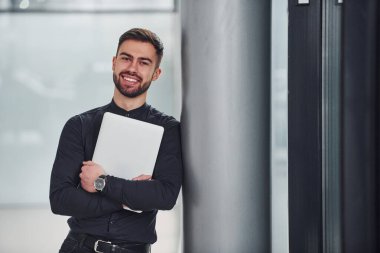 Gri arka planda duran zarif elbiseli genç sakallı adam..