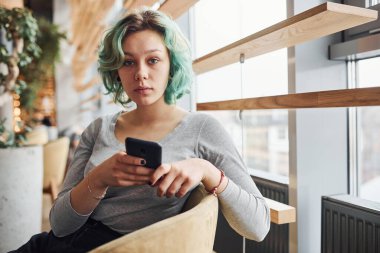 Alternatif kız, yeşil saçlı, gündüz vakti evde oturan, elinde telefon olan..