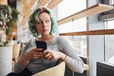 Alternatif kız, yeşil saçlı, gündüz vakti evde oturan, elinde telefon olan..