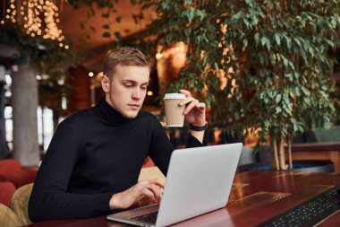 Başarılı genç adam üzerinde dizüstü bilgisayarı olan bir kafede oturuyor..