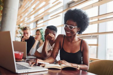Çok ırklı ve yeşil saçlı alternatif bir kız grubunun önünde oturan siyahi kadın kapalı alanda birlikte çalışıyor..