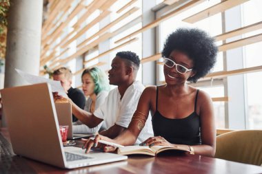 Çok ırklı ve yeşil saçlı alternatif bir kız grubunun önünde oturan siyahi kadın kapalı alanda birlikte çalışıyor..