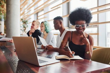 Çok ırklı ve yeşil saçlı alternatif bir kız grubunun önünde oturan siyahi kadın kapalı alanda birlikte çalışıyor..