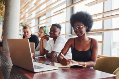 Çok ırklı ve yeşil saçlı alternatif bir kız grubunun önünde oturan siyahi kadın kapalı alanda birlikte çalışıyor..