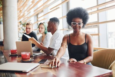 Çok ırklı ve yeşil saçlı alternatif bir kız grubunun önünde oturan siyahi kadın kapalı alanda birlikte çalışıyor..