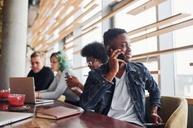 Çok ırklı insanların önünde oturan, yeşil saçlı, alternatif bir kız olan siyahi adam kapalı alanda birlikte çalışıyor..