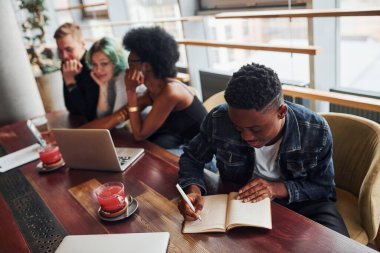 Çok ırklı insanların önünde oturan, yeşil saçlı, alternatif bir kız olan siyahi adam kapalı alanda birlikte çalışıyor..