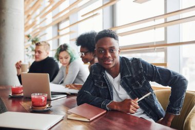 Çok ırklı insanların önünde oturan, yeşil saçlı, alternatif bir kız olan siyahi adam kapalı alanda birlikte çalışıyor..