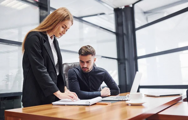 Resmi giyinmiş bir kadın ve bir adam ofis içinde masa başında birlikte çalışıyorlar..