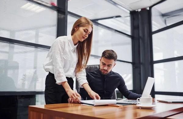 Resmi giyinmiş bir kadın ve bir adam ofis içinde masa başında birlikte çalışıyorlar..