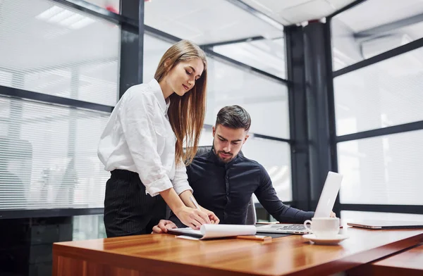 Resmi giyinmiş bir kadın ve bir adam ofis içinde masa başında birlikte çalışıyorlar..