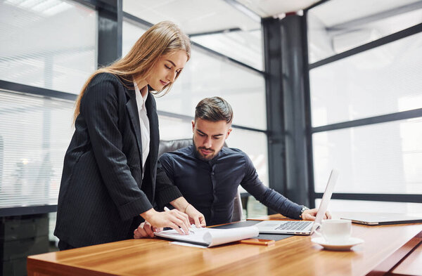 Woman and man in formal clothes working together indoors in the office by table.