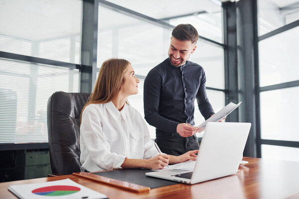 Woman and man in formal clothes working together indoors in the office by table.