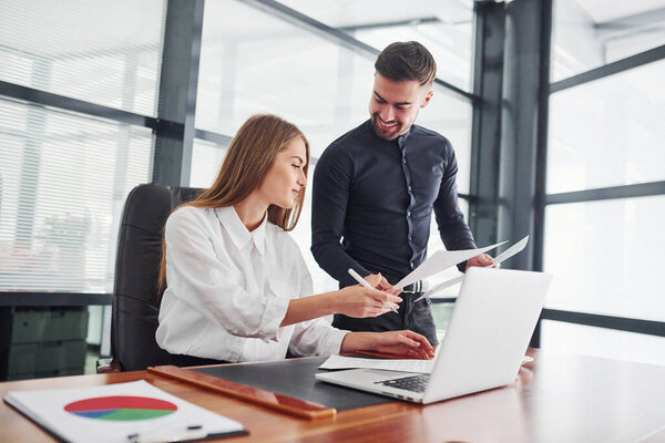 Woman and man in formal clothes working together indoors in the office by table.