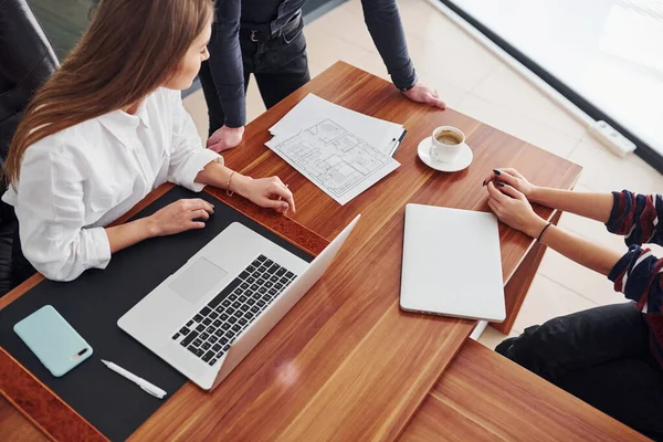 Ofiste laptopla ve belgelerle çalışan üç kişinin üst görüntüsü.