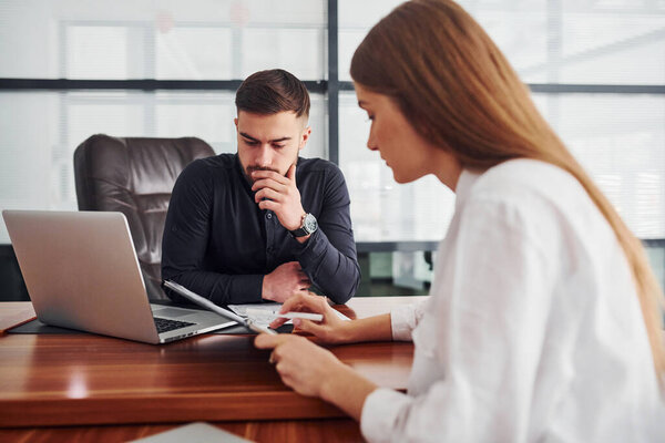 Woman and man in formal clothes working together indoors in the office by table with documents.