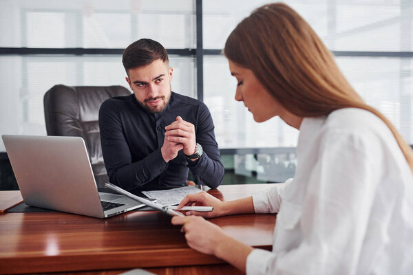 Woman and man in formal clothes working together indoors in the office by table with documents.