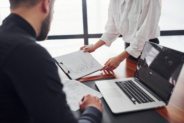 Woman and man in formal clothes working together indoors in the office by table with documents.