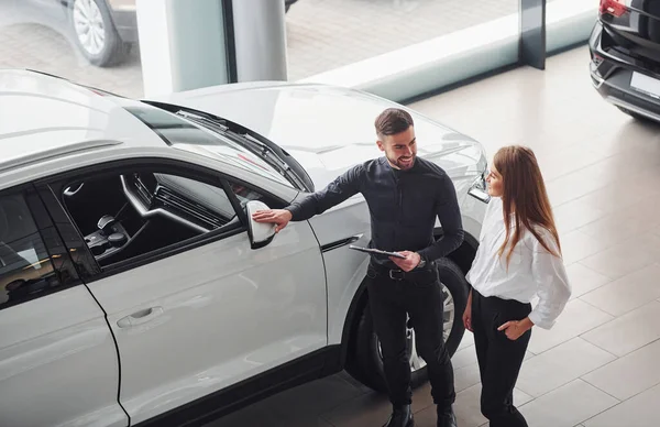 Woman choosing car by help of male assistant indoors in the salon.