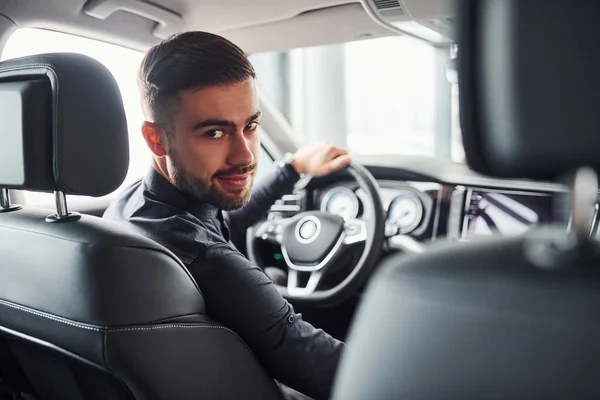 Man in elegant clothes sitting in brand new expencive automobile.