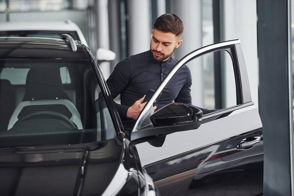 Young man in formal clothes is near brand new expensive car.