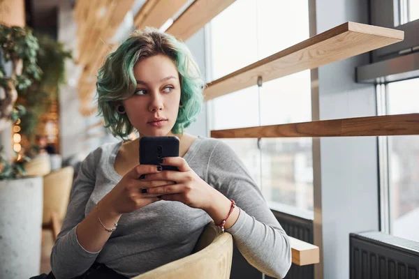 Alternatif kız, yeşil saçlı, gündüz vakti evde oturan, elinde telefon olan..