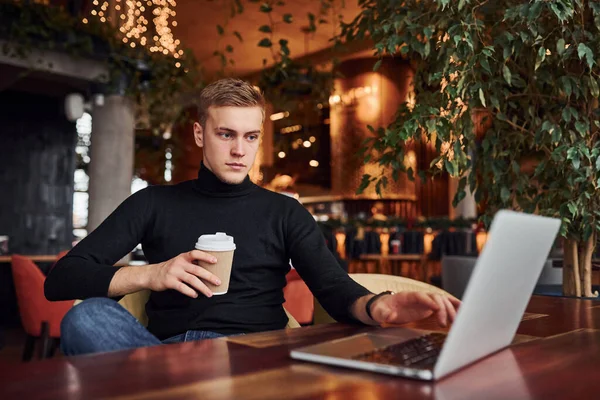 一个成功的年轻人坐在咖啡店旁边 桌上有他的笔记本电脑 — 图库照片