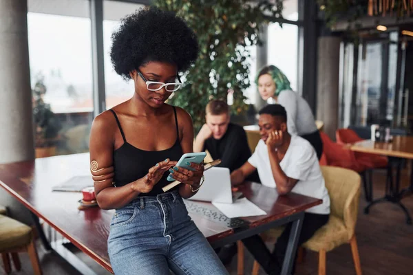 Çok ırklı ve yeşil saçlı alternatif bir kız grubunun önünde duran siyahi kadın kapalı alanda birlikte çalışıyor..