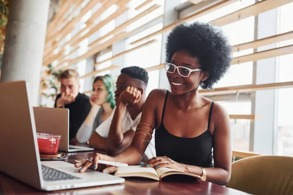 Çok ırklı ve yeşil saçlı alternatif bir kız grubunun önünde oturan siyahi kadın kapalı alanda birlikte çalışıyor..