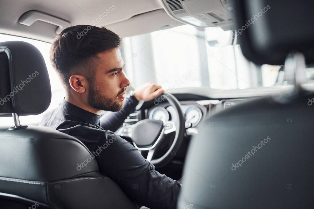 Man in elegant clothes sitting in brand new expencive automobile.