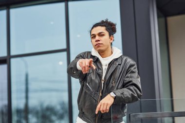Handsome young man with curly black hair is on the street against building.