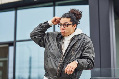 Kıvırcık siyah saçlı ve gözlüklü yakışıklı genç adam caddede binaya karşı..