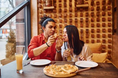 Çok ırklı genç bir çift evde oturup pizza yiyor..