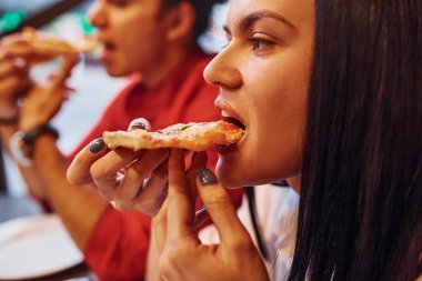 Çok ırklı genç bir çift evde oturup pizza yiyor..