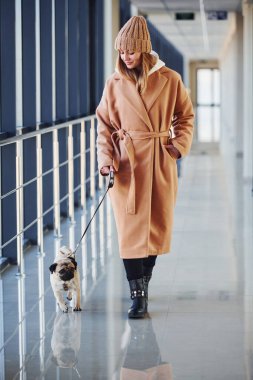 Sıcak giysiler içinde küçük köpeğiyle koridorda yürüyen bir kadın..