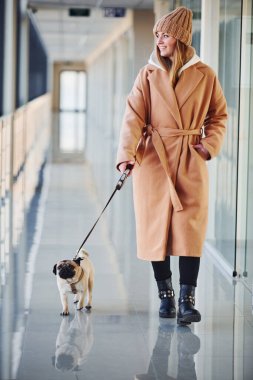 Sıcak giysiler içinde küçük köpeğiyle koridorda yürüyen bir kadın..