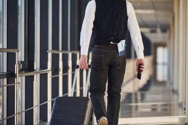 Rear view of male passenger in elegant formal clothes is in the airport hall with tickets in his pocket.