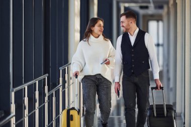 Resmi şık elbiseli bir adam havaalanında genç bir bayanla yürüyor..