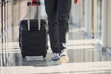 Grounded view of male passenger in elegant formal clothes is in the airport hall walking with baggage.
