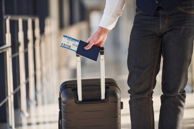 Close up view of male passenger in elegant formal clothes that is in the airport hall with baggage and tickets.