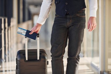 Close up view of male passenger in elegant formal clothes that is in the airport hall with baggage and tickets.